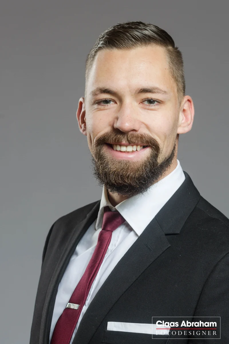 Bewerbungsporträt mit dunklem Anzug und roter Krawatte.