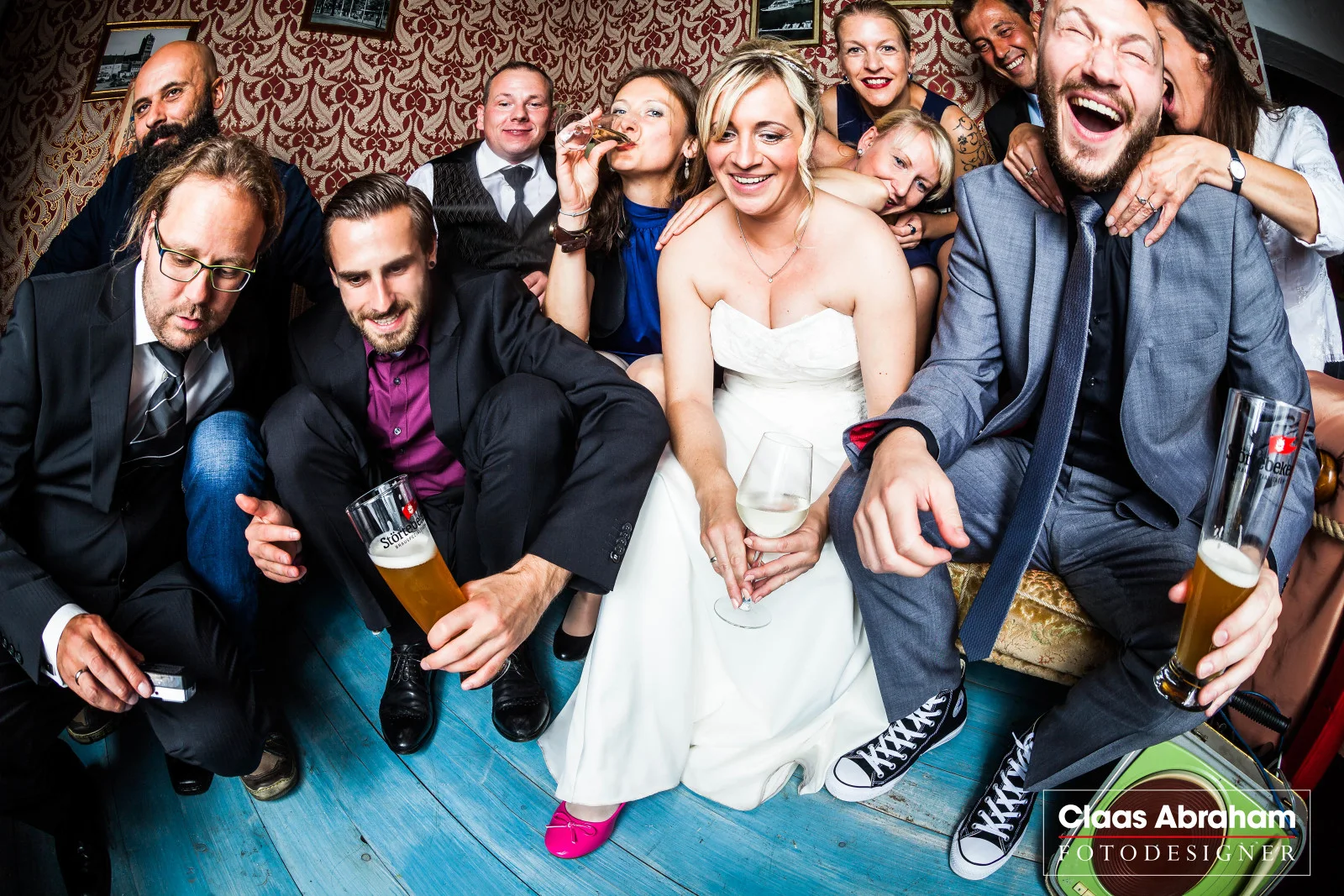 Eine große Hochzeitsgruppe lacht gemeinsam vor der Fotoboxkamera.